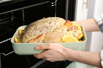 Photo of Woman putting raw chicken with orange slices into oven, closeup