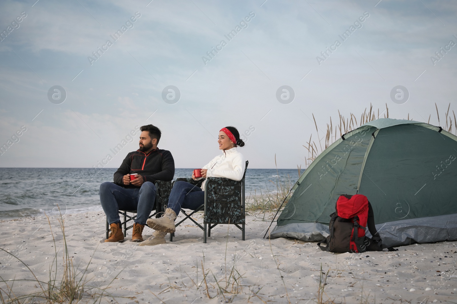 Photo of Couple with hot drinks near camping tent on beach