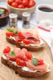 Photo of Tasty bruschettas with prosciutto, tomatoes and cheese on white wooden table, closeup