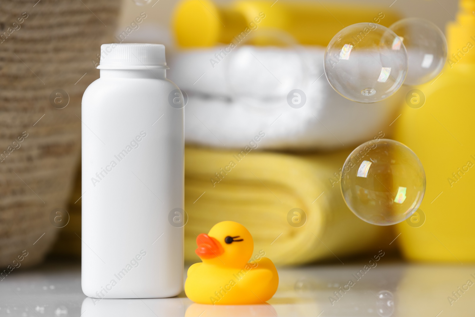 Photo of Bottle of dusting powder and rubber duck on white table, space for text. Baby cosmetic product