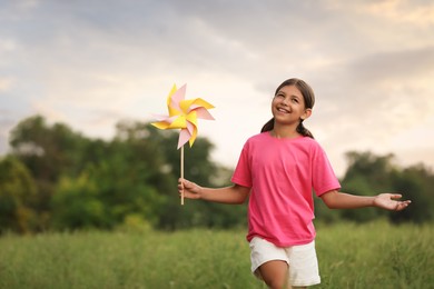 Cute little girl with pinwheel in field, space for text. Child spending time in nature