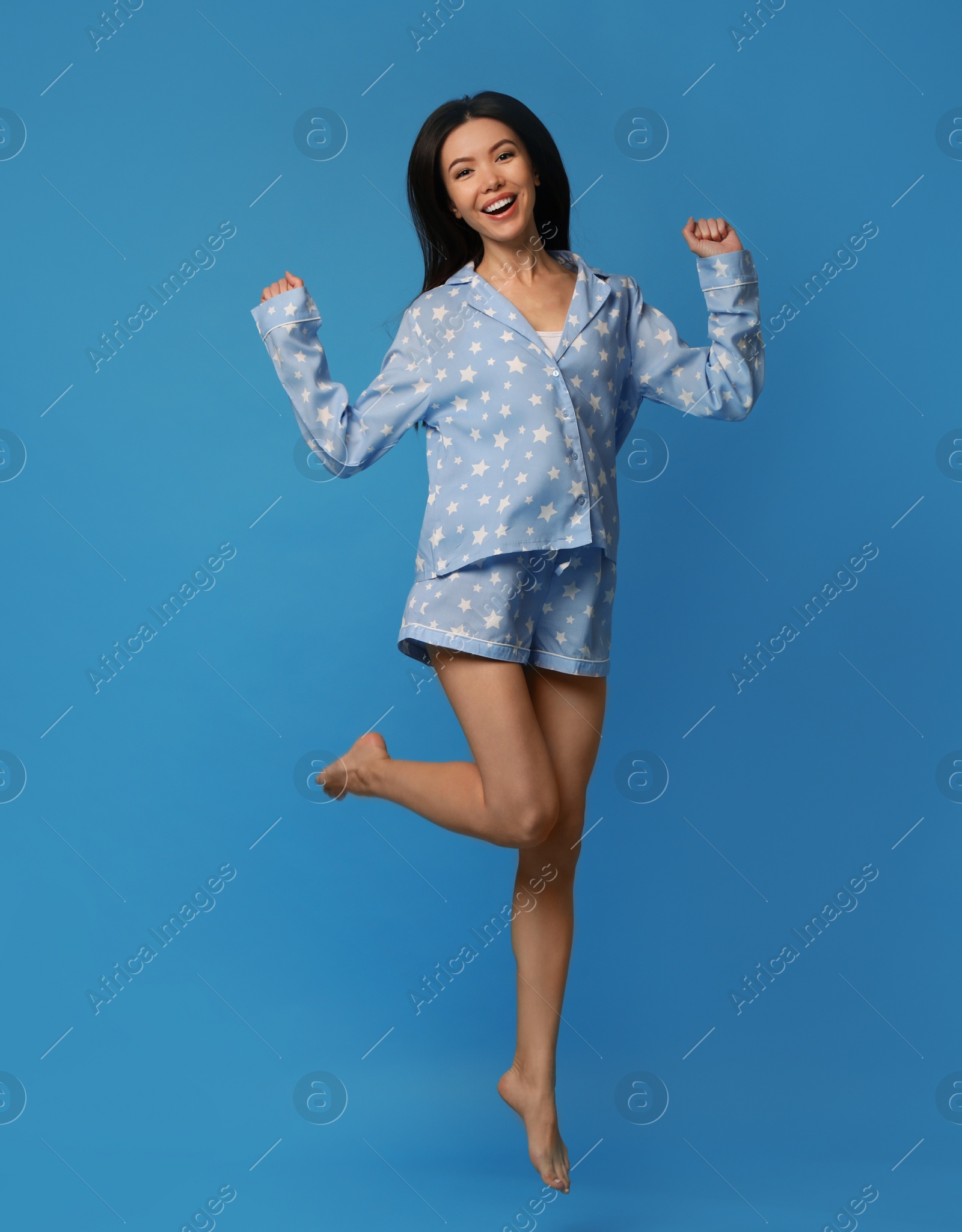 Photo of Beautiful Asian woman in pajamas jumping on blue background. Bedtime