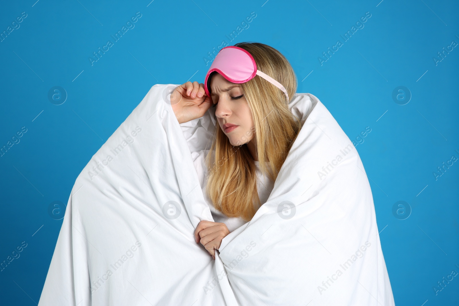 Photo of Young woman in sleeping mask wrapped with soft blanket on blue background