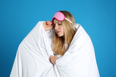 Photo of Young woman in sleeping mask wrapped with soft blanket on blue background
