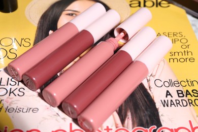 Bright lip glosses and fashion magazine on table, closeup