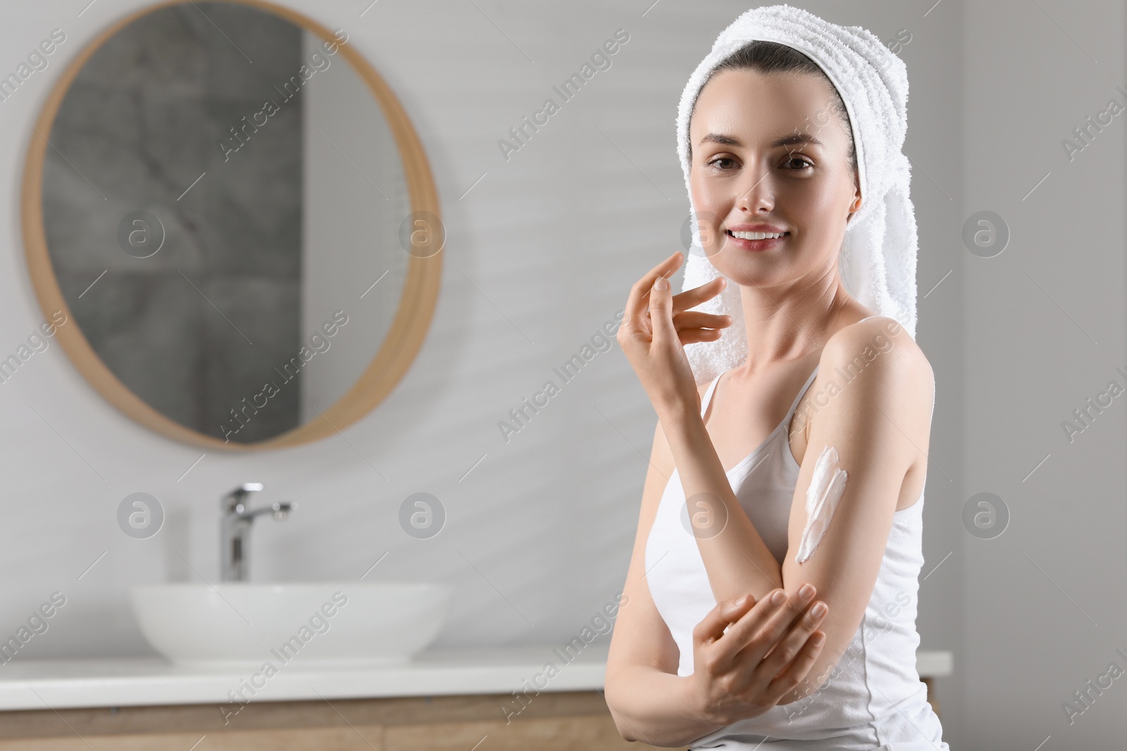 Photo of Happy woman applying body cream onto arm in bathroom, space for text