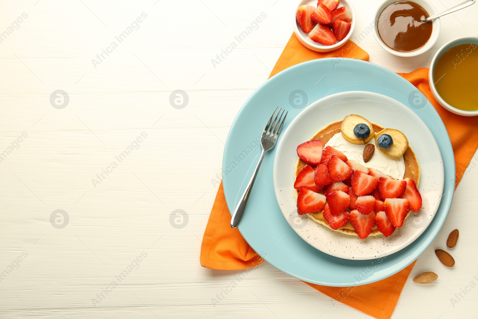 Photo of Creative serving for kids. Plate with cute owl made of pancakes, strawberries, cream, banana and almond on white wooden table, flat lay. Space for text