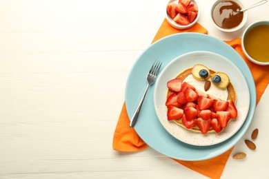 Photo of Creative serving for kids. Plate with cute owl made of pancakes, strawberries, cream, banana and almond on white wooden table, flat lay. Space for text