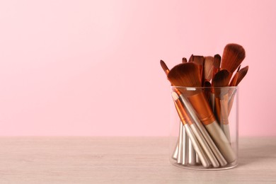 Photo of Set of professional makeup brushes on wooden table against pink background, space for text