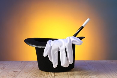 Photo of Magician's hat, wand and gloves on wooden table against color background