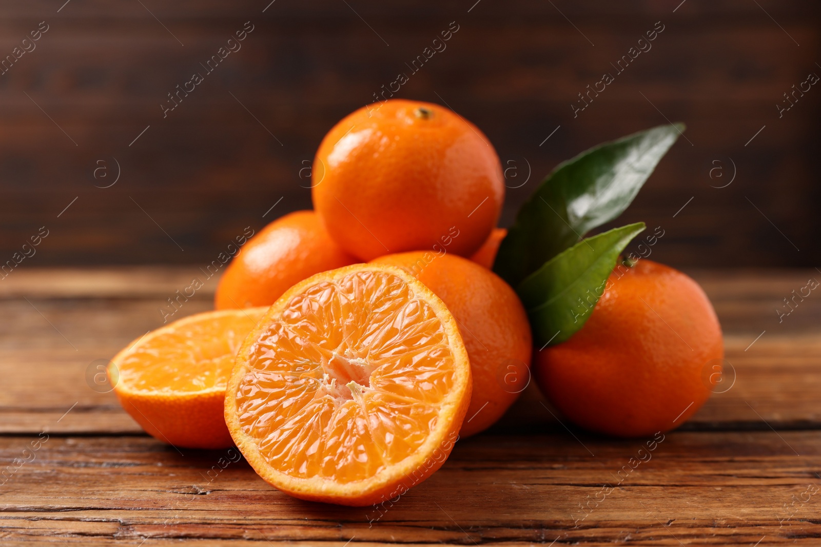 Photo of Fresh tangerines with green leaves on wooden table, closeup