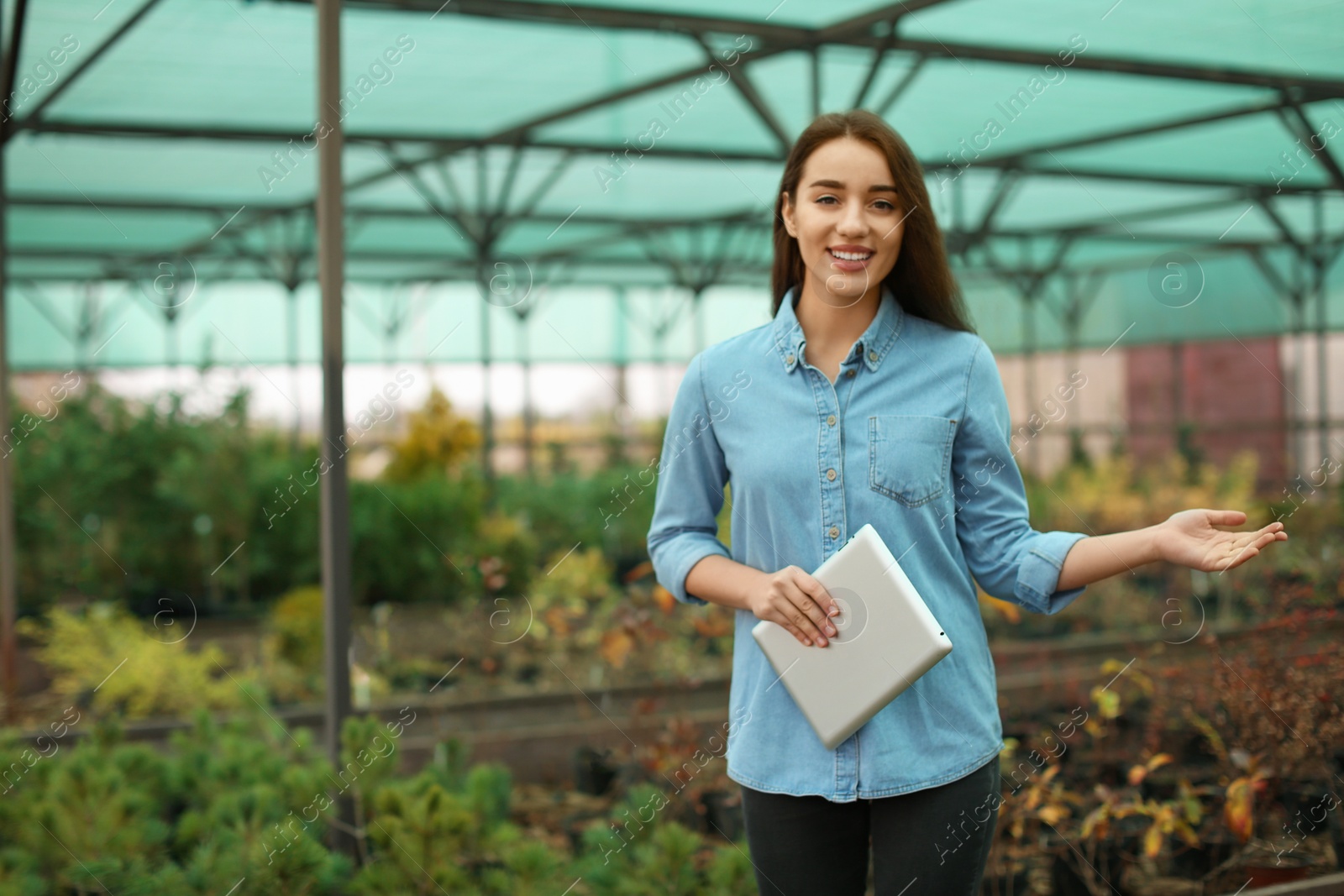 Photo of Female business owner with tablet showing her greenhouse. Space for text