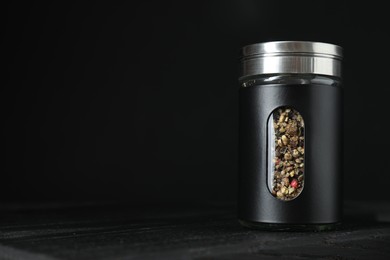 Photo of Pepper shaker on wooden board against black background. Space for text