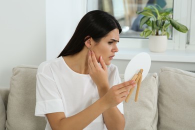 Photo of Young woman looking in mirror and touching her face at home. Hormonal disorders