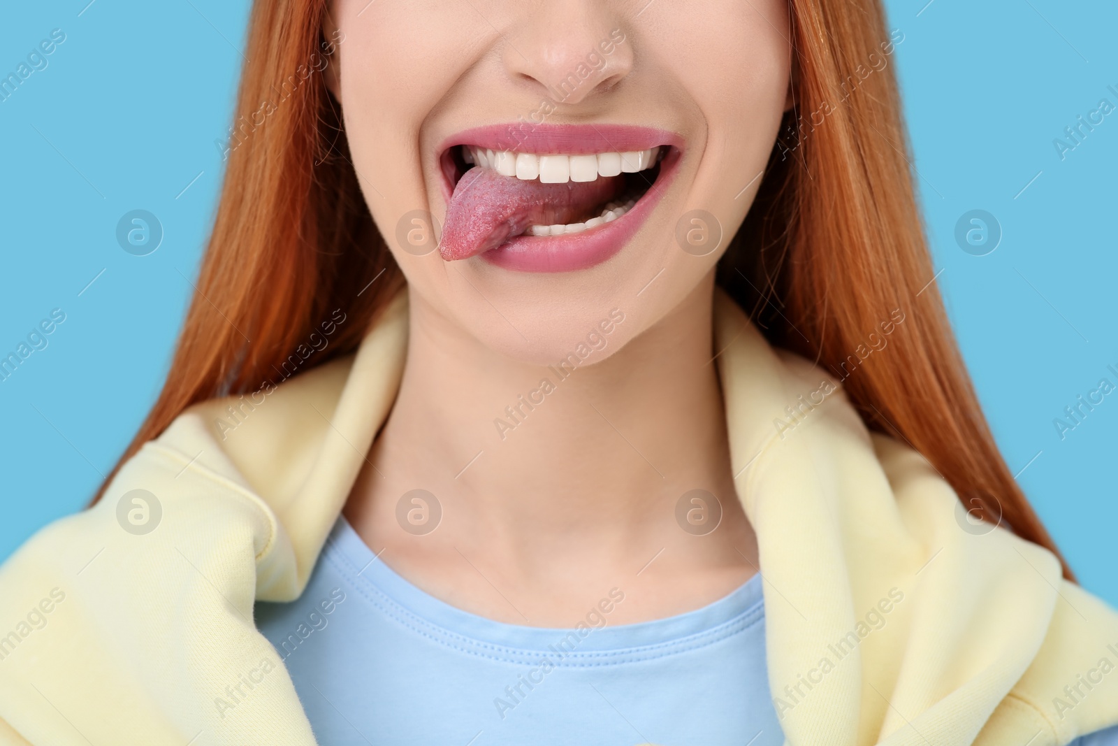 Photo of Happy woman showing her tongue on light blue background, closeup