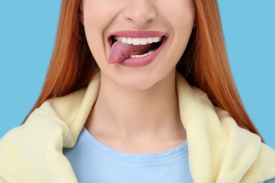 Happy woman showing her tongue on light blue background, closeup