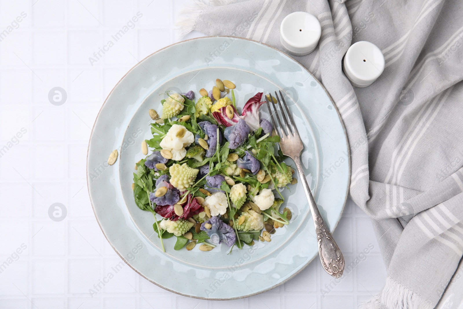 Photo of Delicious salad with cauliflower and pumpkin seeds served on white tiled table, flat lay