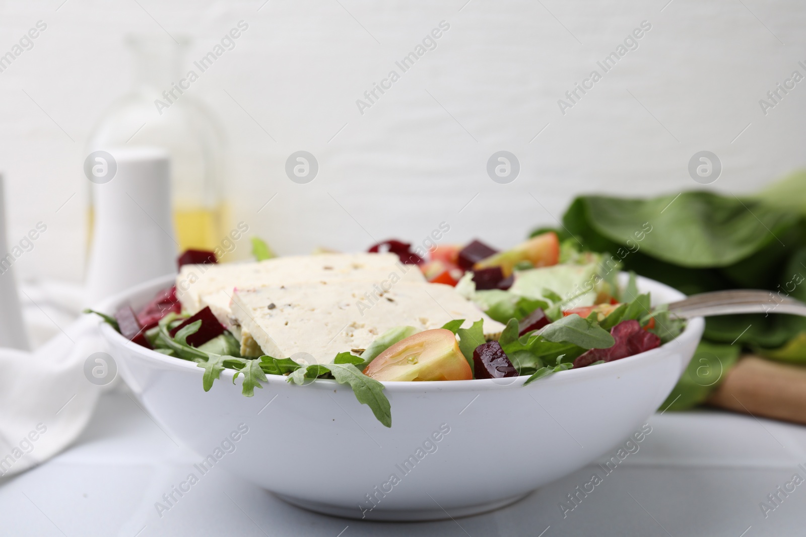 Photo of Bowl of tasty salad with tofu and vegetables on white tiled table, closeup