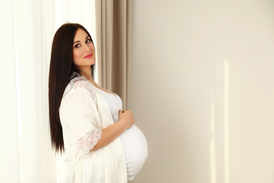 Beautiful pregnant woman near window at home. Space for text