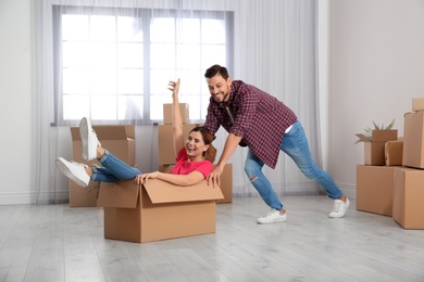 Photo of Happy couple playing with cardboard box in their new house. Moving day
