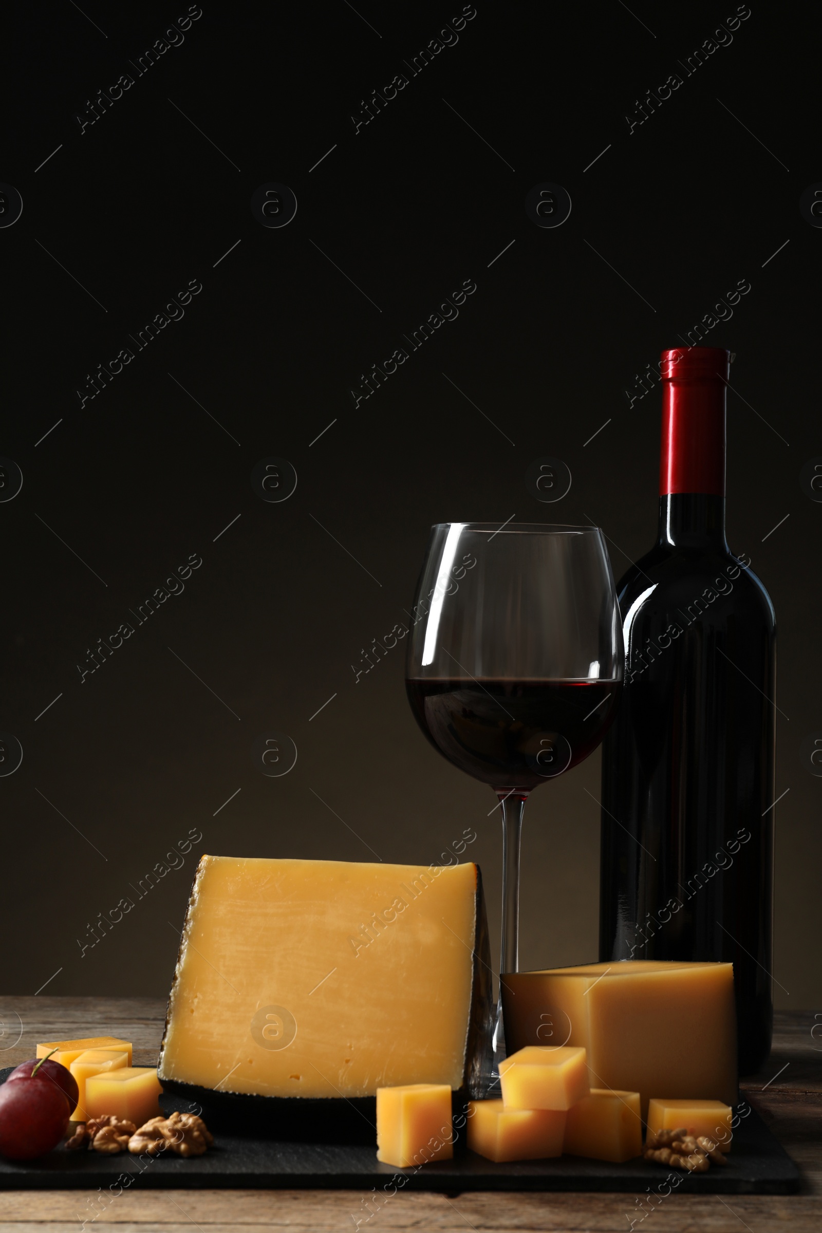 Photo of Delicious cheese served with red wine on table against dark background