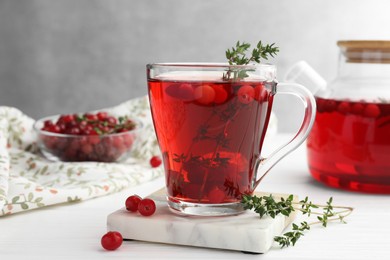 Photo of Tasty hot cranberry tea with thyme and fresh berries in glass cup on white wooden table