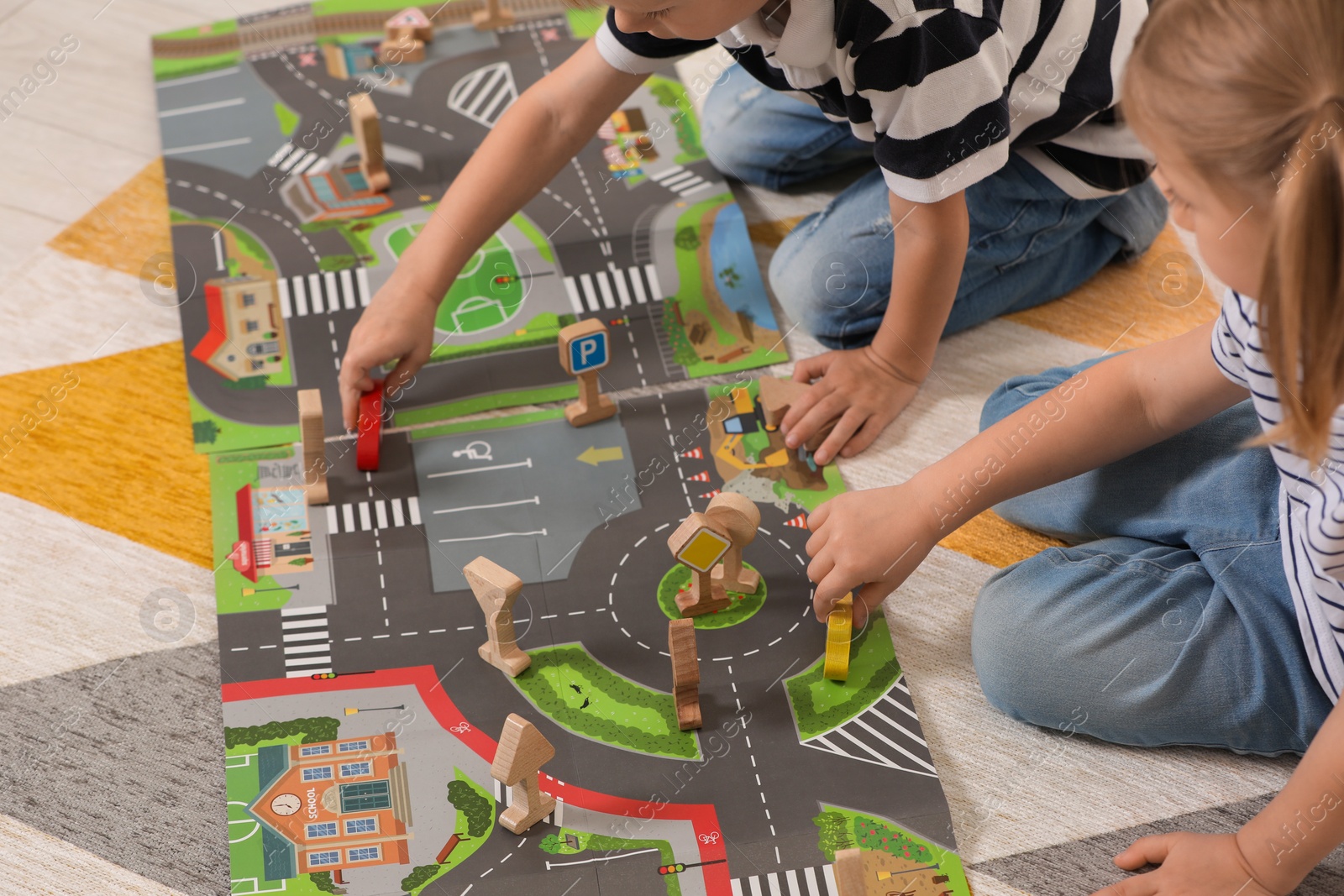 Photo of Little children playing with set of wooden road signs and toy cars indoors, closeup