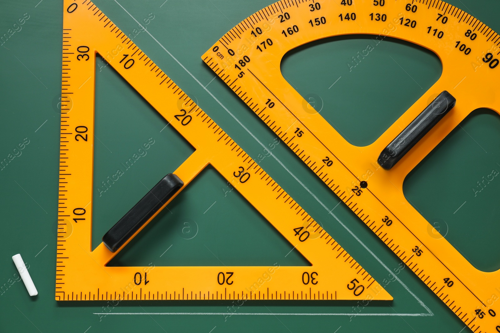 Photo of Protractor, triangle and chalk on green chalkboard, flat lay