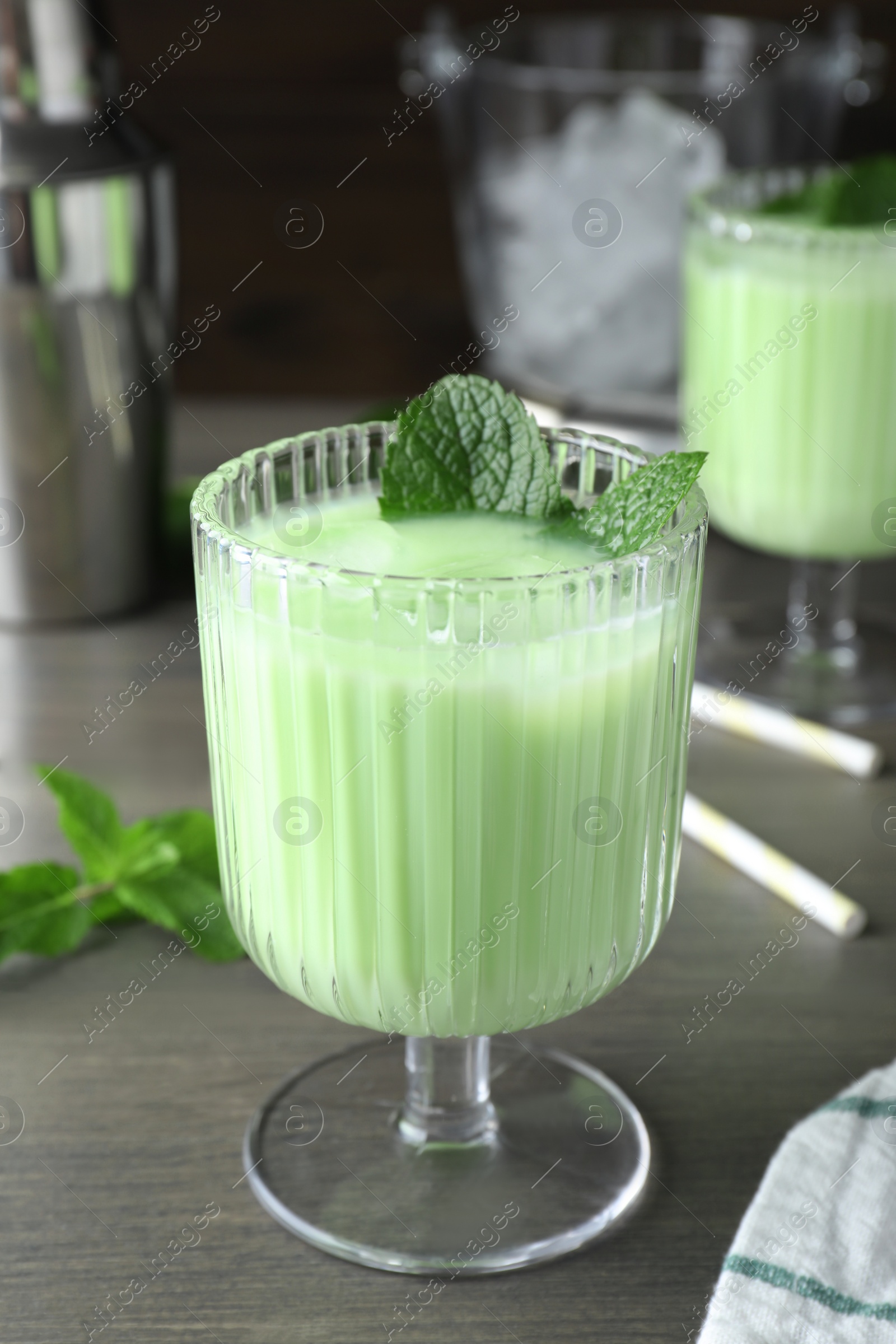 Photo of Delicious mint liqueur with ice cubes and green leaves on grey wooden table, closeup