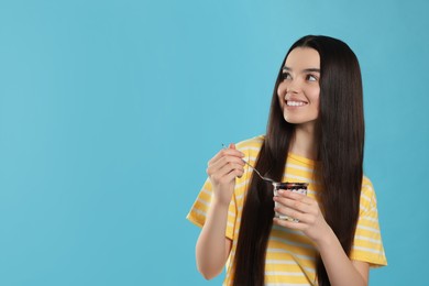 Photo of Happy teenage girl with delicious yogurt and spoon on light blue background. Space for text