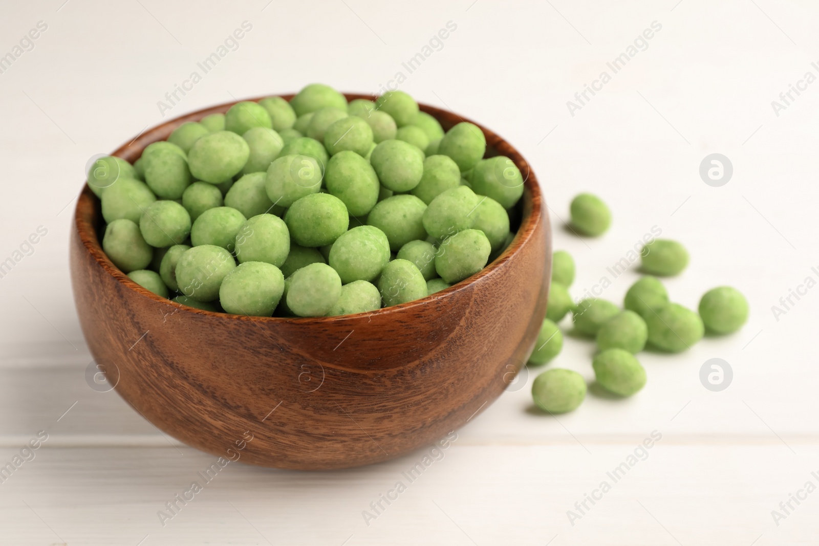 Photo of Bowl with tasty wasabi coated peanuts on white wooden table, closeup. Space for text