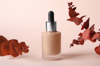 Photo of Bottle of skin foundation and decorative branches on beige background. Makeup product