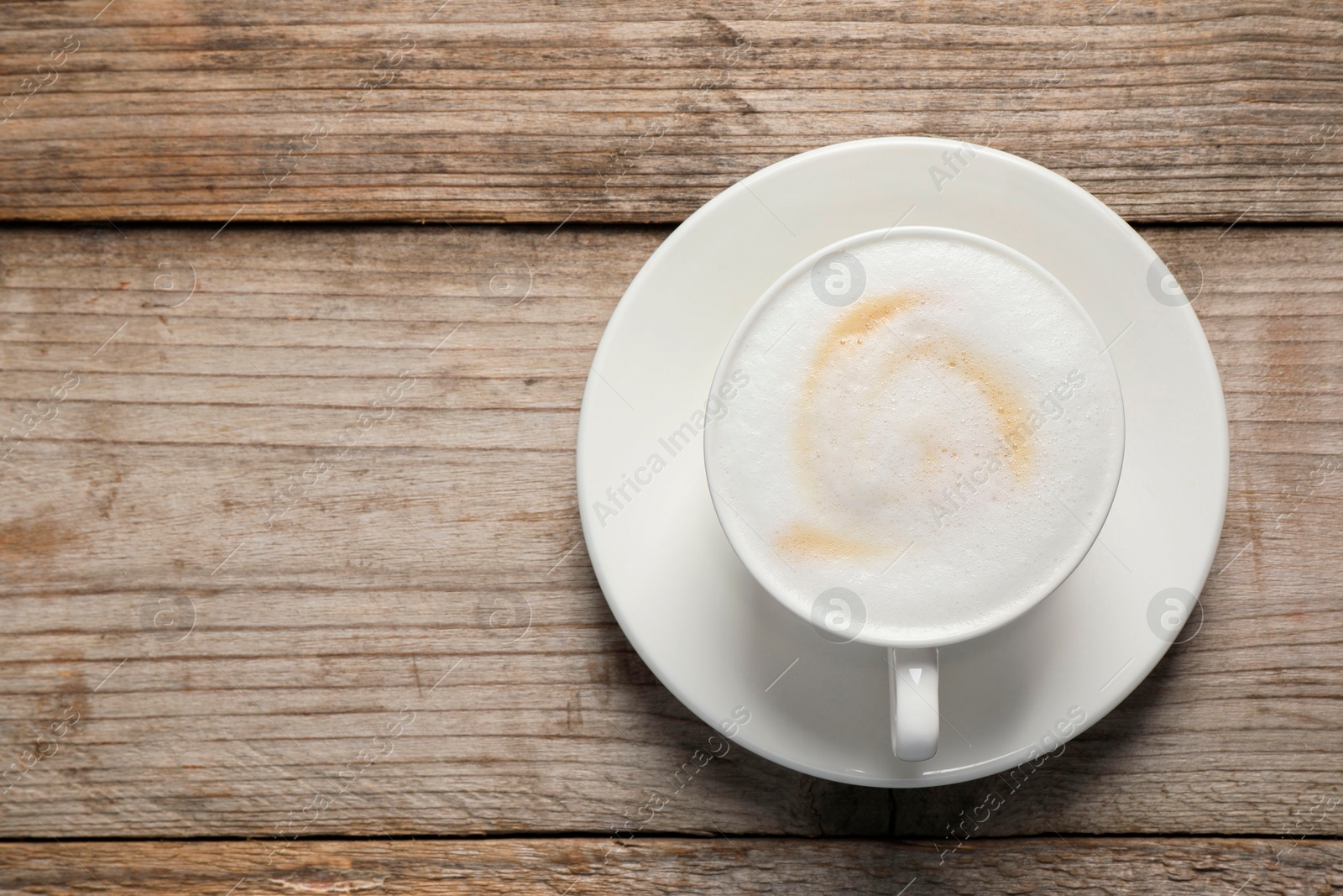 Photo of Tasty cappuccino in coffee cup on wooden table, top view. Space for text