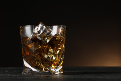 Photo of Whiskey and ice cubes in glass on black table, closeup. Space for text