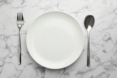 Photo of Empty plate, fork and spoon on white marble table, top view