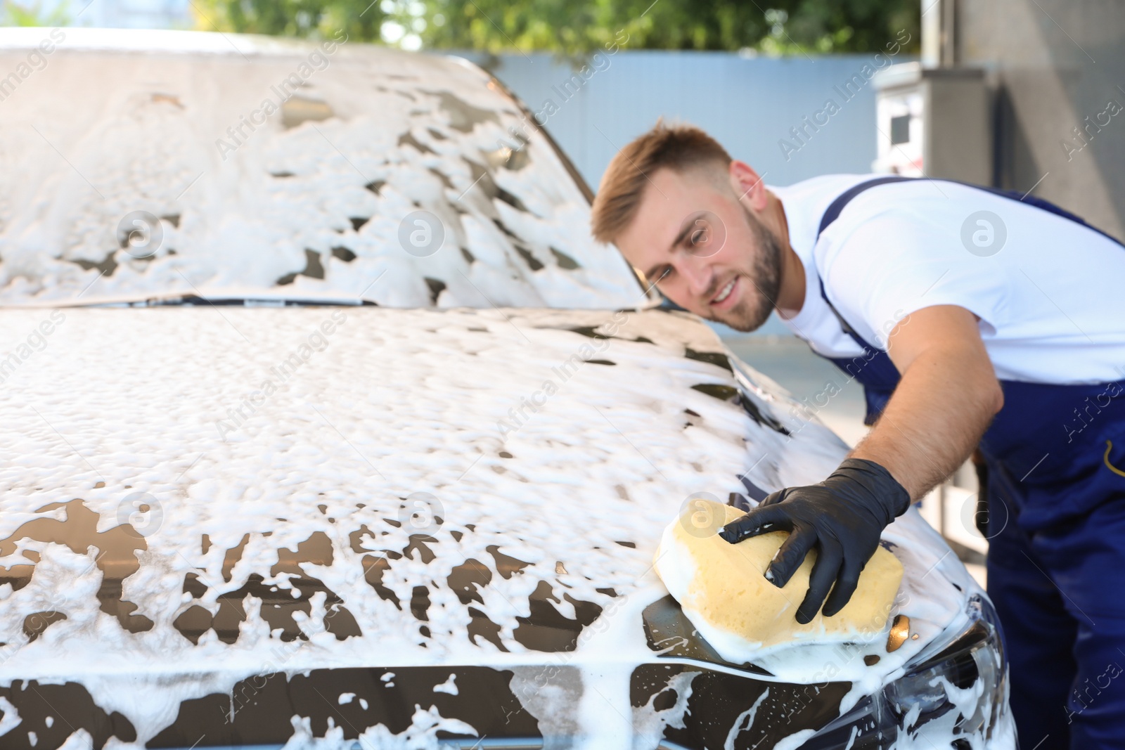 Photo of Young worker cleaning automobile with sponge at car wash