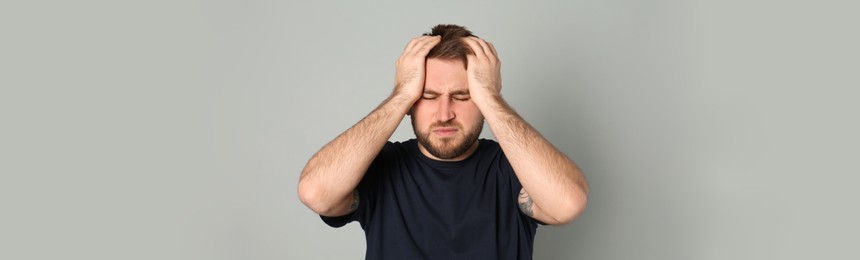 Image of Tired man suffering from migraine on grey background. Banner design