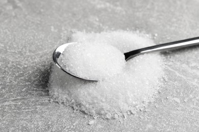 Granulated sugar and spoon on light grey table, closeup