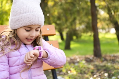 Photo of Little girl using modern smart watch outdoors