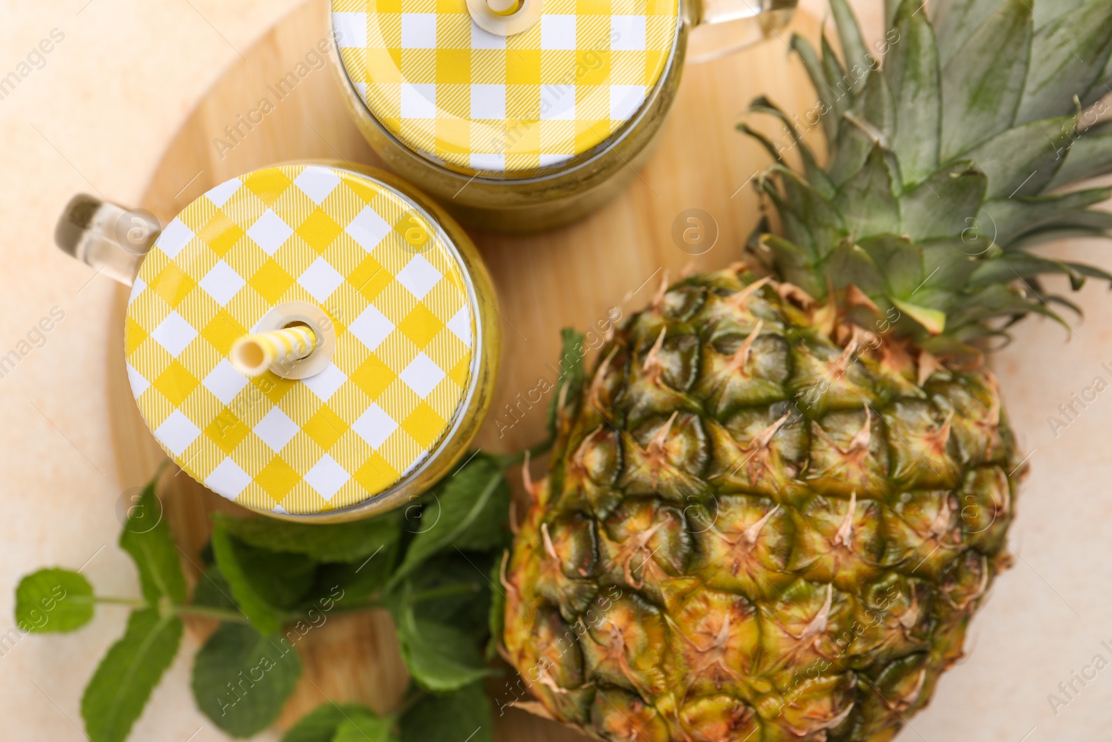 Photo of Tasty pineapple smoothie in mason jars, mint and fruit on beige table, flat lay