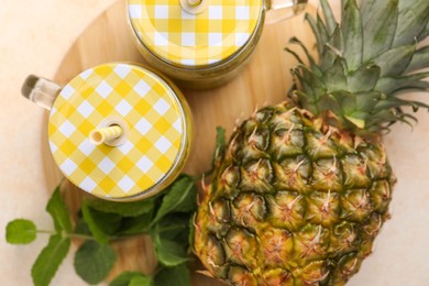 Tasty pineapple smoothie in mason jars, mint and fruit on beige table, flat lay