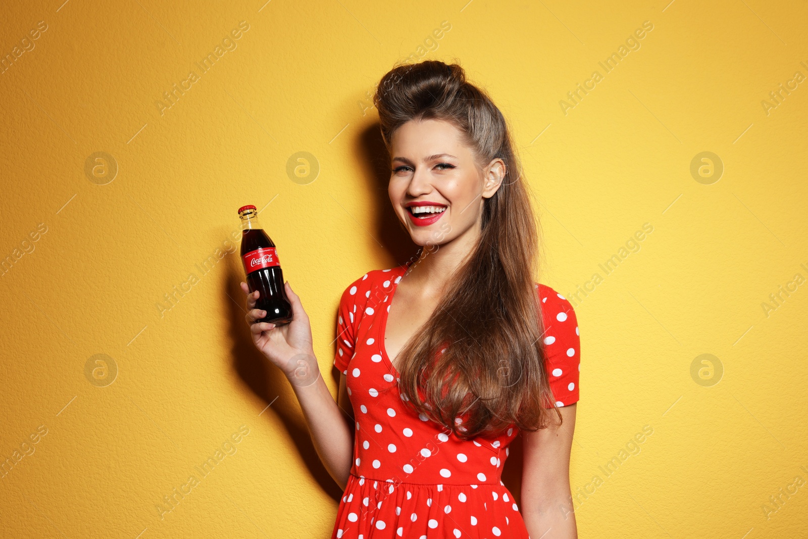 Photo of MYKOLAIV, UKRAINE - NOVEMBER 28, 2018: Young woman with bottle of Coca-Cola on color background