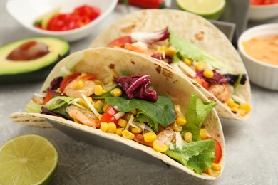 Photo of Delicious tacos with shrimps and lime on light grey table, closeup