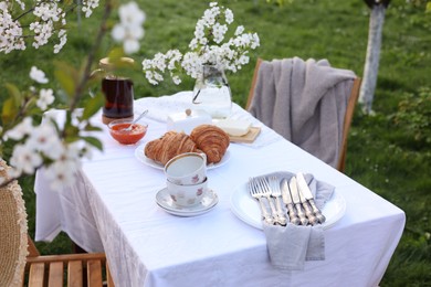 Photo of Stylish table setting with beautiful spring flowers, tea and croissants in garden