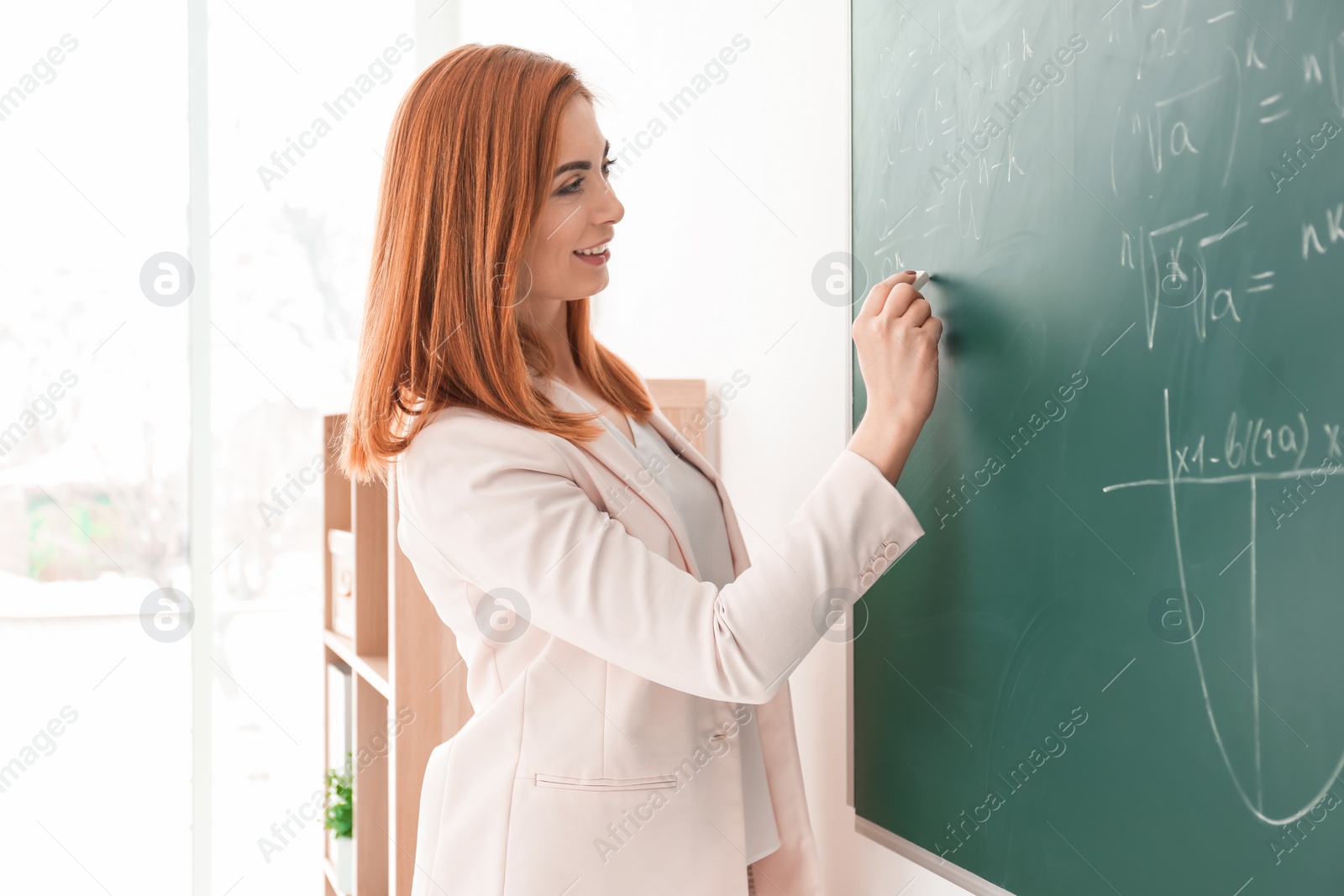 Photo of Beautiful young teacher writing on blackboard in classroom