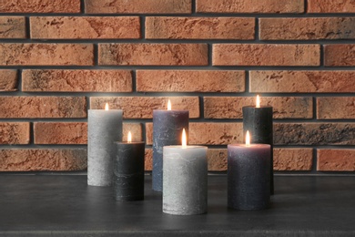 Photo of Burning candles on table against brick wall