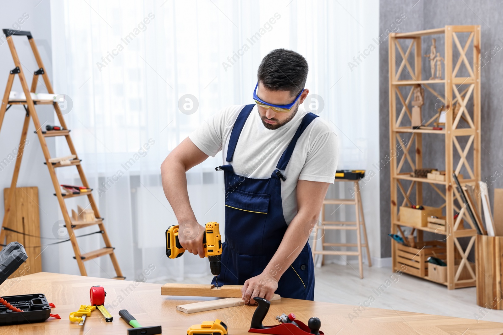 Photo of Young worker using electric drill at table in workshop