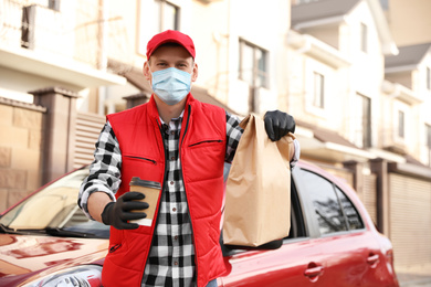 Courier in protective mask and gloves with orders near car outdoors. Food delivery service during coronavirus quarantine