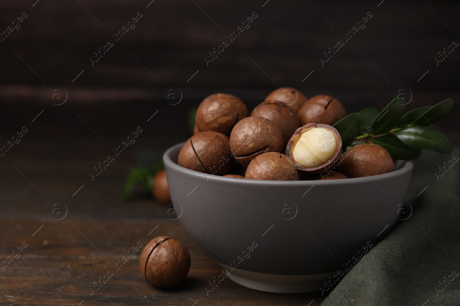 Photo of Tasty Macadamia nuts and green twig in bowl on wooden table. Space for text