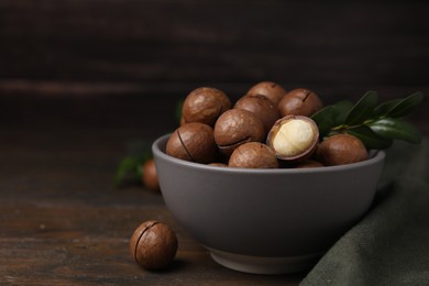 Photo of Tasty Macadamia nuts and green twig in bowl on wooden table. Space for text